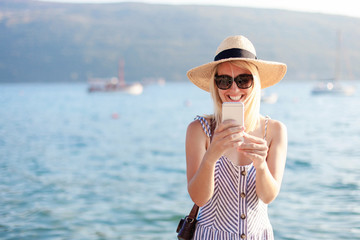 Woman traveler is using mobile phone at summer beach. Female tourist takes photos of sea,...