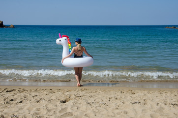 Woman standing on beach with inflatable unicorn pool float near sea © Marharyta