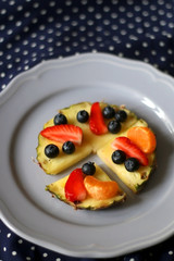 Various spring fruit on a lilac plate: strawberries, pineapple, blueberries and tangerine. Polka dot background. Selective focus.