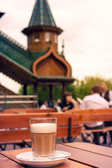 A glass of hot tasted latte with a spoon on a wooden table.
