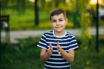 A little boy in a striped T-shirt standing in front of green background. Smiling and looking to the...
