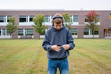 Fototapeta premium Happy teenager standing in the middle of a soccer field while listening to some music on an overcast day.