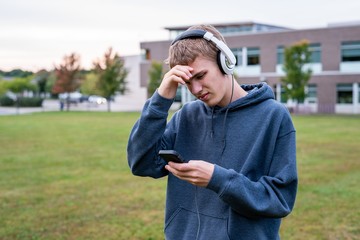 Upset teenager listening to music with his headphones on an overcast day.