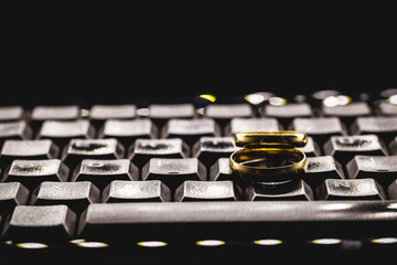 golden wedding rings on a personal computer keyboard. Concept of infidelity or virtual betrayal.