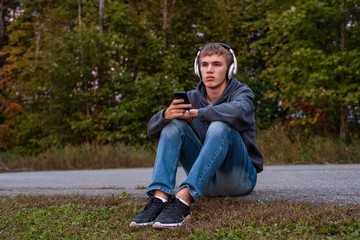 Obraz premium Upset teenager sitting on the ground all alone while listening to some music.