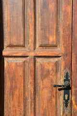Old, wooden, dilapidated door with a brass handle, lighted by sunlight. Retro styled door in light brown color. Doors details. Closeup