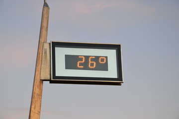Outdoor thermometer indicating the high temperature - 26 degrees. Sky before sunset with slightly...