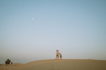 Father with two daughter standing on a sand dune in the desert with a moon on the beackground