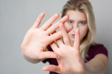 Young blonde girl showing stop gesture over grey wall. Space for text