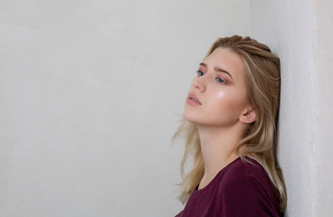 Sad blonde girl standing near the grey wall. Space for text