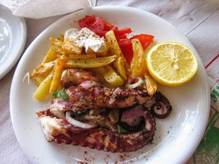 Pieces of grilled octopus on white plate with french fries and lemon piece