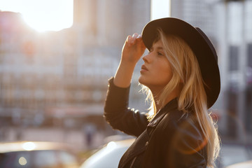 Gorgeous blonde woman wearing black hat posing at sunset with sun glare. Empty space