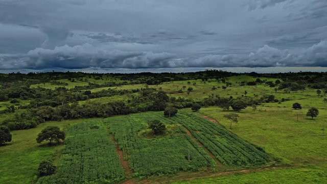 Dark moody aerial shot over green fields in the Brazil countryside on a stormy day. Forward Dolly shot