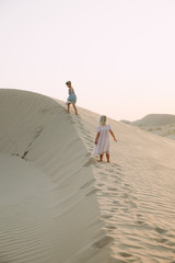 Fototapeta premium Two little girl walking on sand dunes in the desert in Dubai