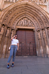 Fototapeta na wymiar A young brunette woman walking in front of the Cathedral of Valencia (Spain) with white shirt and gray pants