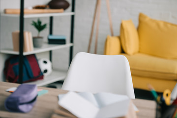 selective focus of desk with copy books and stationery, rack and yellow sofa