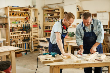 Portrait of two carpenters working with wood standing at table in workshop, copy space