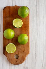 Whole and cut green citrus limes on a rustic wooden board over white wooden surface, top view. Flat lay, overhead, from above. Copy space.