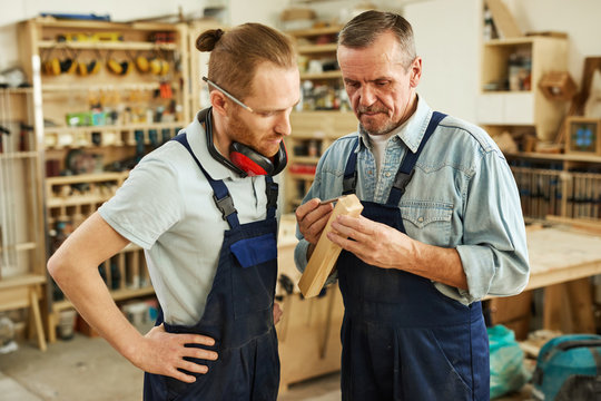 Waist up portrait of senior carpenter teaching apprentice  standing  in joinery workshop, copy space
