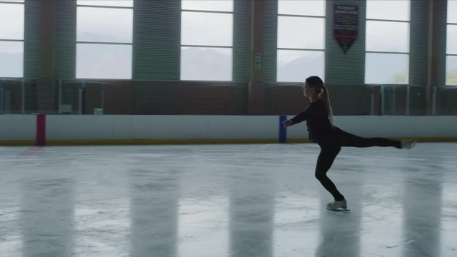 Slow motion of woman figure skating on ice skating rink and jumping / Murray, Utah, United States