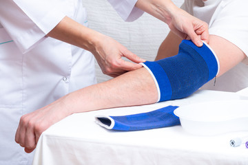 doctor helps the patient to use bandage on the elbow