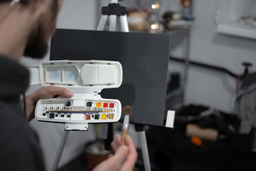Young man painting with brush and watercolor on easel
