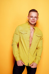 Positive young sexy male in trendy yellow shirt looking at camera on yellow background.