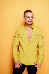 Positive young sexy male in trendy yellow shirt looking at camera on yellow background.