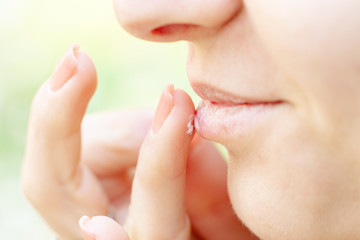 Obraz premium woman applying lip balm. outdoor, blurred green background. authentic photo. side view. skin care concept.