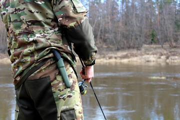 Fototapeta premium Angler in camouflage clothing, fishing on spinning
