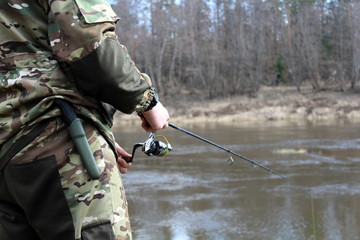 Fisherman in camouflage clothing, fishing on spinning.