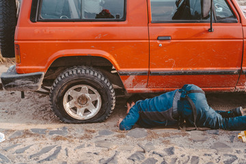 man lies under a 4x4 car on a dirt road