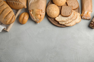 Different kinds of fresh bread on grey table, flat lay. Space for text
