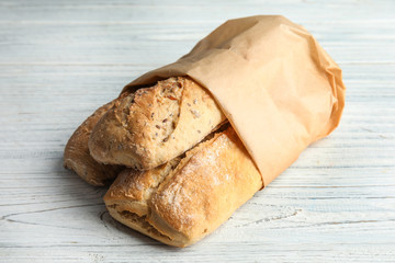 Mini baguettes in paper bag on wooden table, closeup. Wholegrain bread