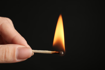 Woman holding burning match on black background, closeup. Space for text