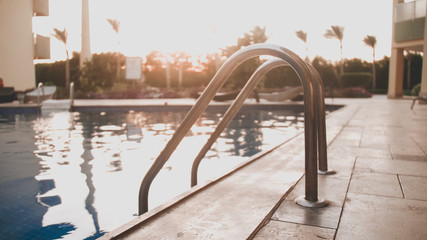 Closeup toned image of metal staircase railings in swimming pool against amazing sunset sky