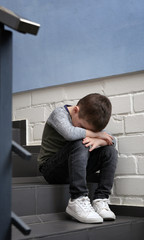 Obraz premium Sad little boy sitting on stairs indoors
