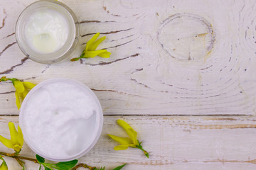 Jar of moisturizer cream with yellow forsythia blossoms on white wooden background. Top view