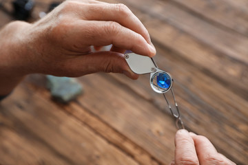 Male jeweler evaluating precious gemstone at table in workshop, closeup