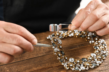 Male jeweler evaluating necklace at table in workshop, closeup