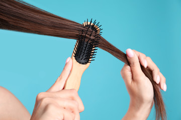 Woman with hair brush on color background, closeup