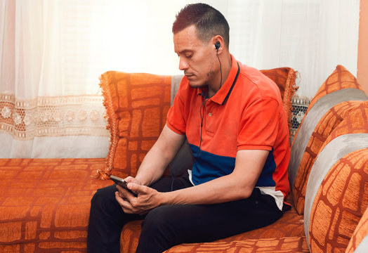 Handsome young men with headphones using his smart phone and sitting on sofa