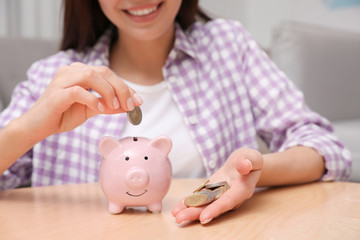 Obraz na płótnie Canvas Happy woman putting coin into piggy bank at home