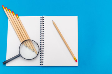 White notepad with steel pen on a blue background. Office table, minimal composition. Magnifying glass. Copy space.