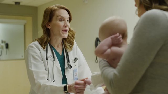 Smiling doctor talking with mother of baby in examination room / Salt Lake City, Utah, United States