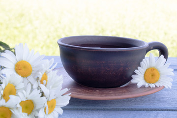Fototapeta na wymiar A cup of tea with daisies stands on a blue table against a background of green grass.