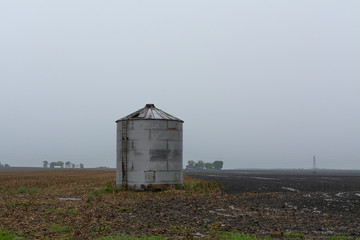 Fototapeta na wymiar Single metal silo on open field as the Spring rain falls.
