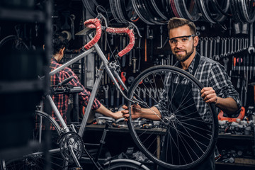 Handsome smiling man in protective glasses is fixing bicycle at his own shop.