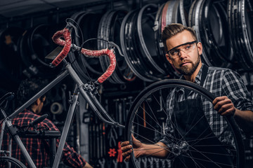 Naklejka na ściany i meble Focused attractive man in glasses is chainging wheel for bicycle at busy workshop.