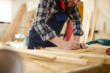 Mid section portrait of unrecognizable carpenter marking wood while working in joinery lit by sunlight, copy space